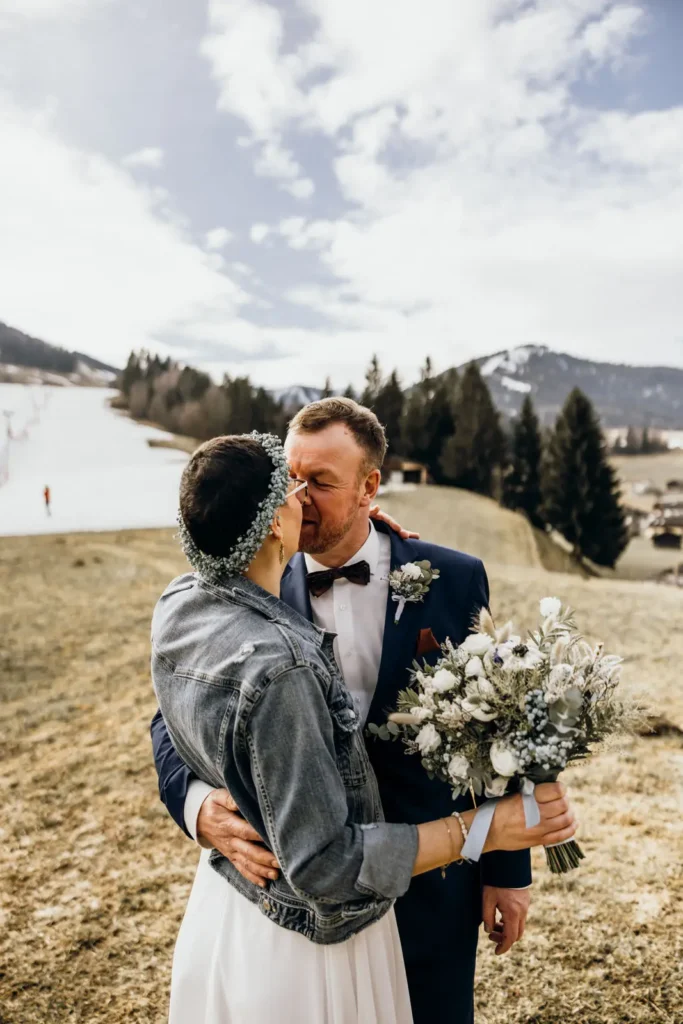 Nach der Hochzeit in den Bergen küssen sich Braut und Bräutigam. Die Braut hält dabei ihren Brautstrauß.