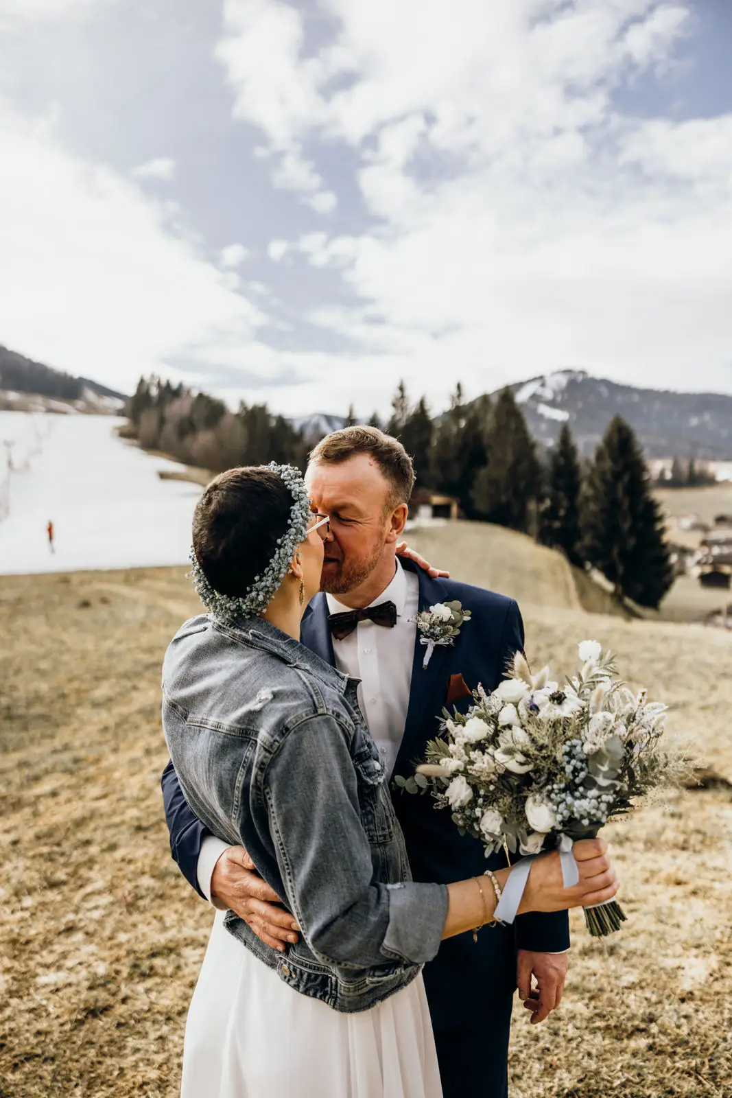 Nach der Hochzeit in den Bergen küssen sich Braut und Bräutigam. Die Braut hält dabei ihren Brautstrauß.
