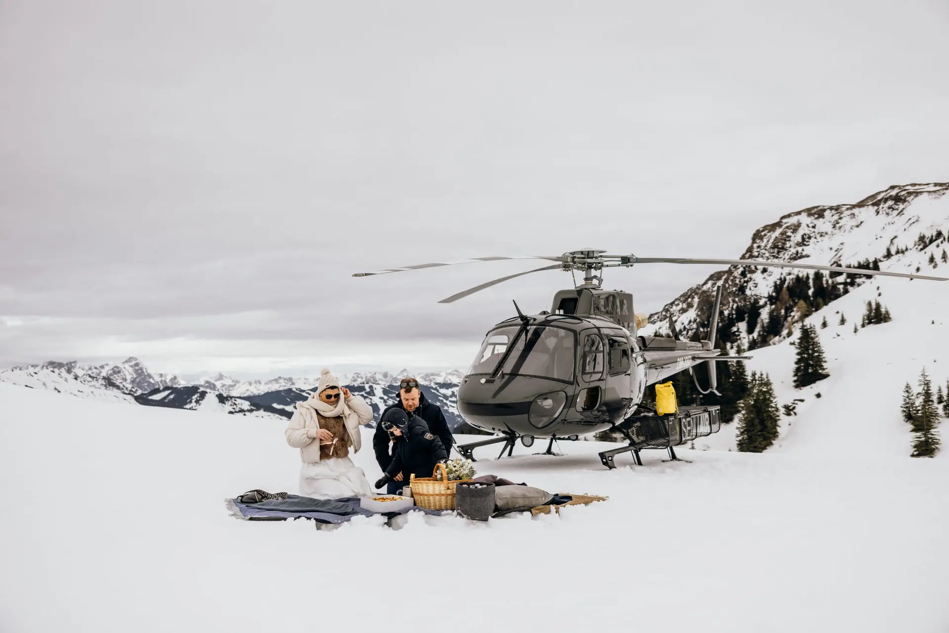 Ein Brautpaar mit Hubschrauber und Kind beim Winterpicknick im Schnee.
