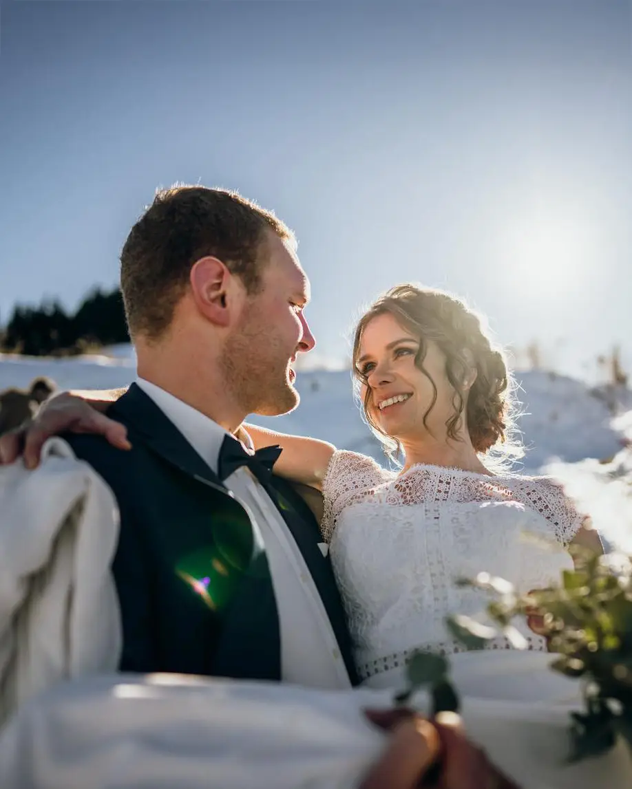 Ein Paar beim Fotoshooting bei ihrer Winterhochzeit zu zweit. Die Sonne strahlt die beiden an während die Braut vom Bräutigam auf Händen getragen wird.