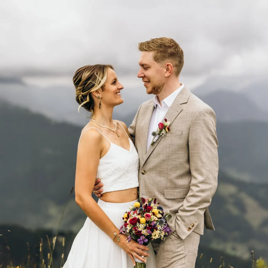 Ein Hochzeitspaar mit einem bunten Brautstrauß passend zur Sommerhochzeit zu zweit in den Bergen.