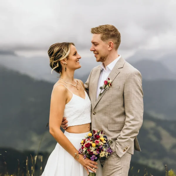 Ein Hochzeitspaar mit einem bunten Brautstrauß passend zur Sommerhochzeit zu zweit in den Bergen.